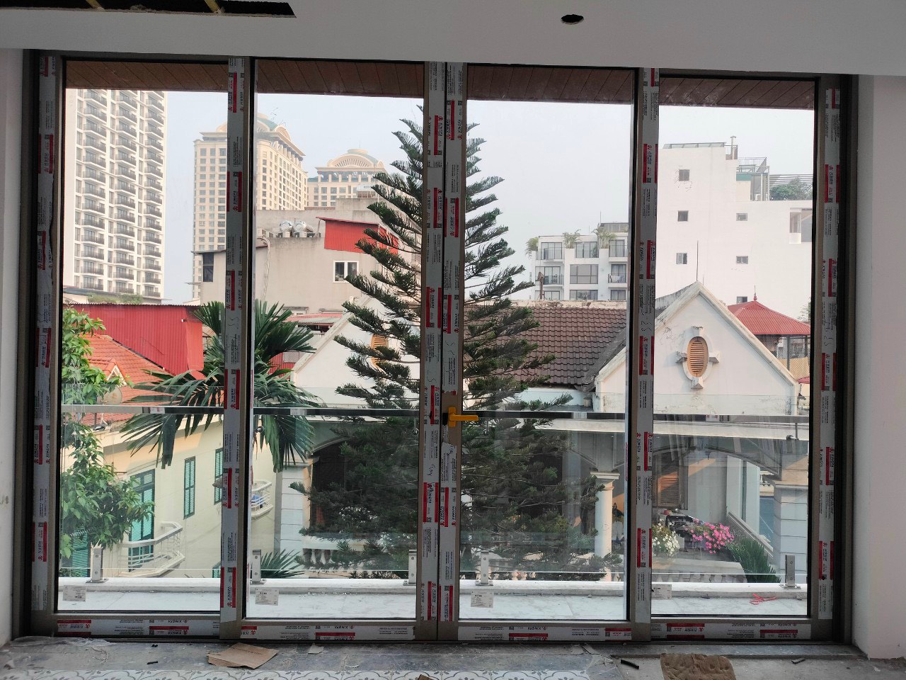 Cửa kính trượt khung nhôm lớn đang lắp đặt, nhìn ra khu nhà phố và cây xanh bên ngoài